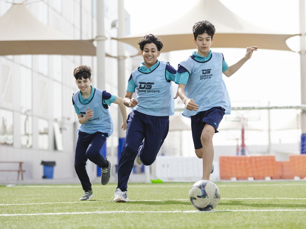 Three pupils running with a football on the pitch
